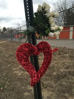crash site memorial with a heart and white roses on pole