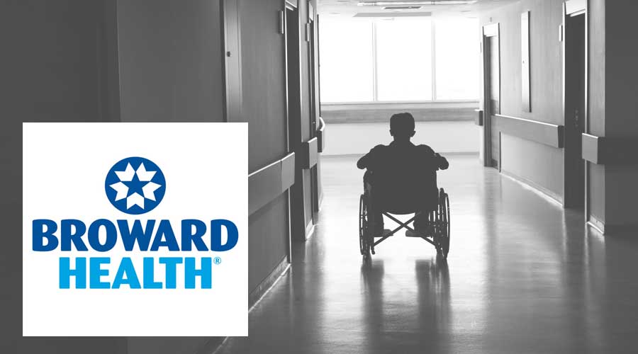 Rear view of man sitting in a wheelchair in a hallway with Broward Health's logo