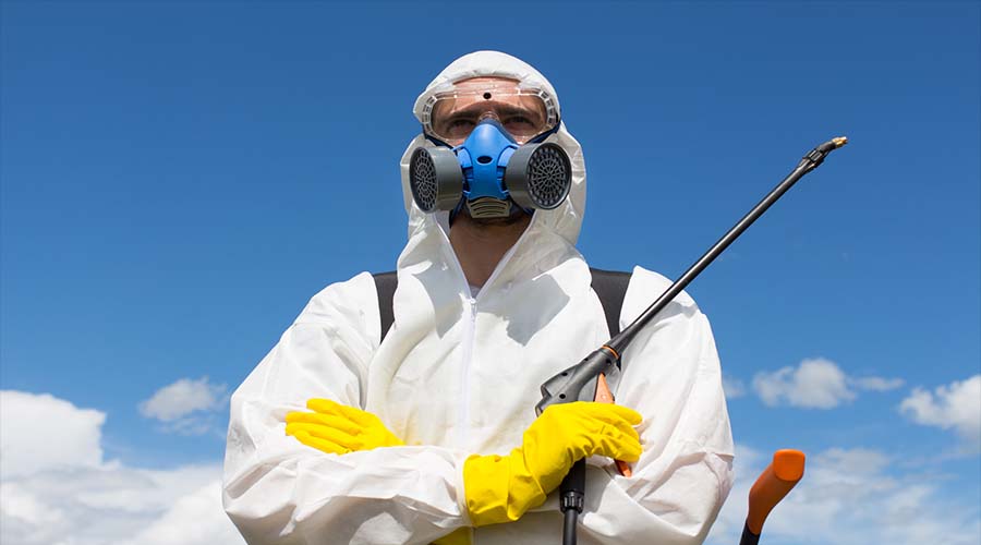 man in protective gear and holding pesticide sprayer